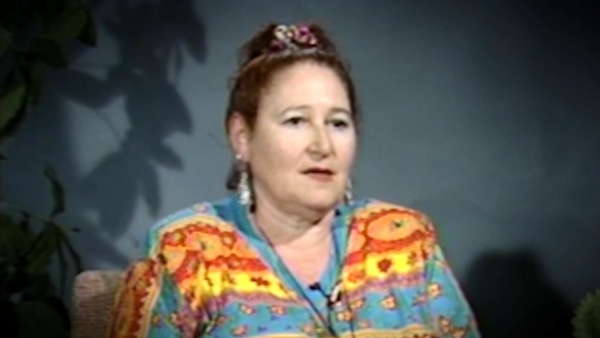 Capture d'écran du témoignage vidéo de la survivante de l’Holocauste Hélène Goldflus, assise devant un fond bleu, et regardant à la droite de la caméra. Son visage et ses épaules sont visibles à la caméra.